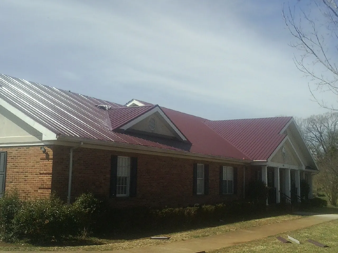 Red metal roof with gabled entries on a long brick building, from a Hail Damage Roof Repair job in Hatboro