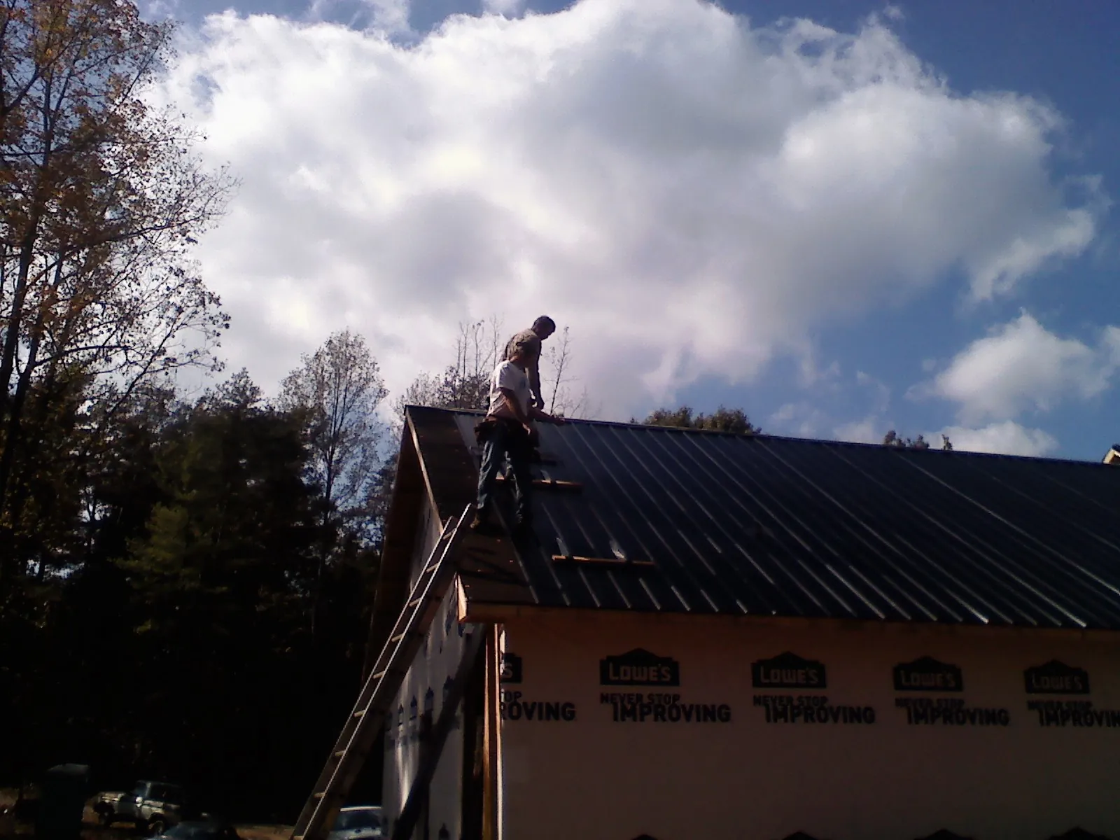 Roofer fastening dark metal panels high against a cloudy sky, from a Roof Inspection job in Hatboro
