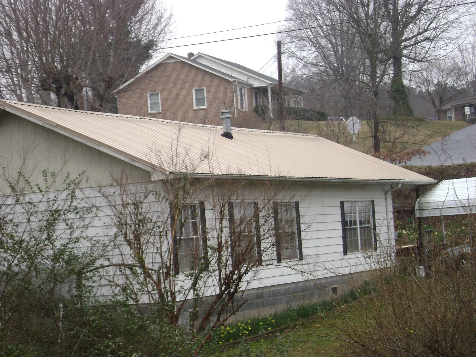 Tan metal roof on a white sided house set into a hillside — Commercial Roofing by Roofing Brothers in Hatboro